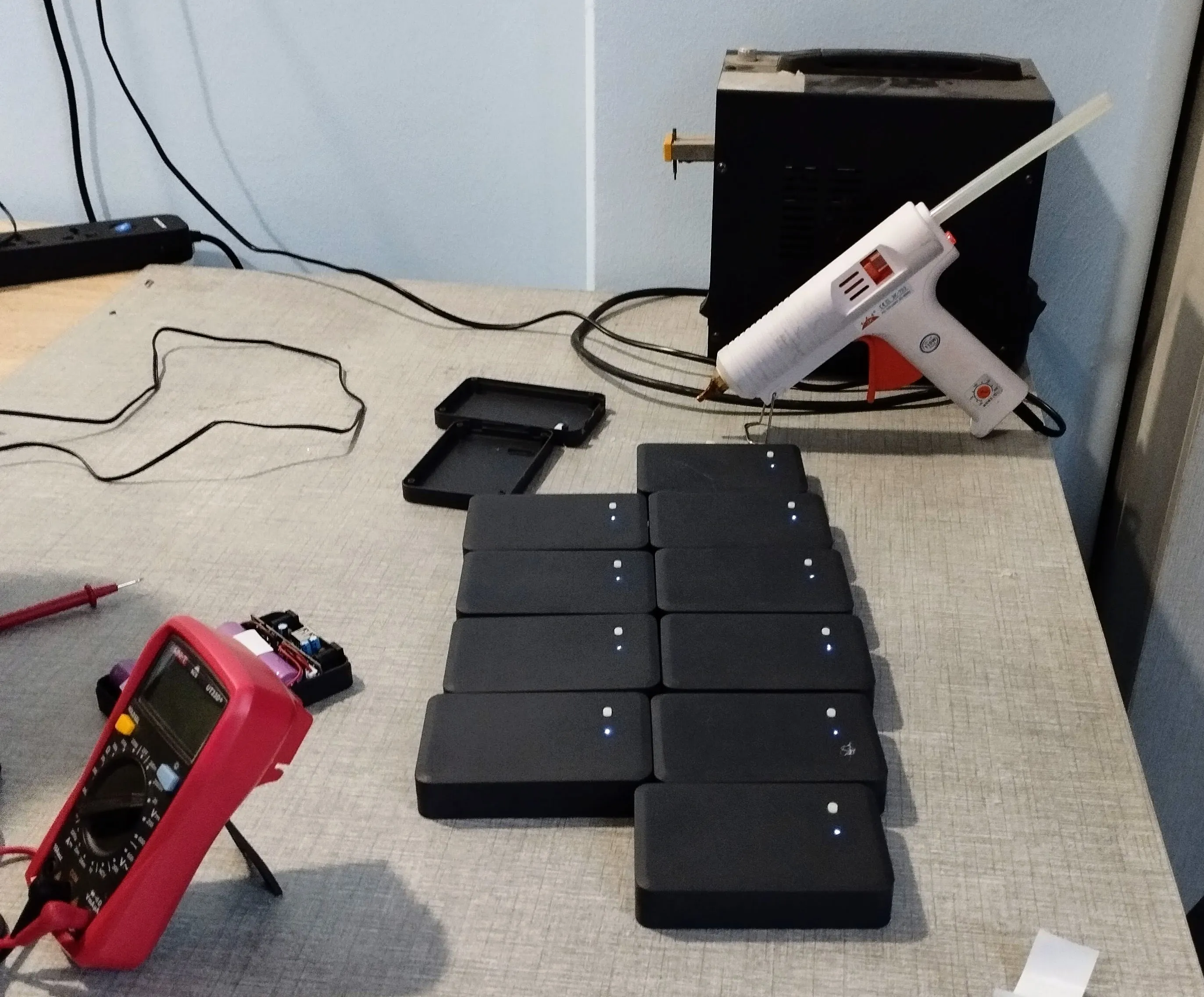 A row of finished units on the bench beside a multimeter and a glue gun
